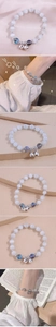 Detail of beaded bracelet with white cat eye stones and silver bell pendant on wrist