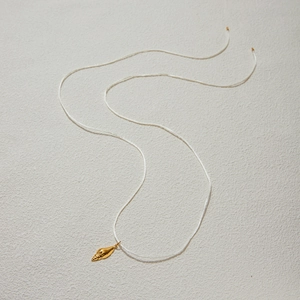 Detail showing a golden conch shell pendant on a white cord for a nautical necklace