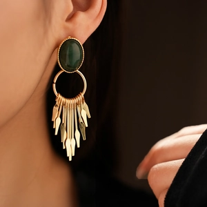 Detail of vintage gold earrings with green gemstones and metal tassel on a model