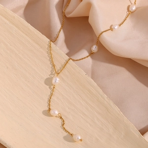 Detail of a gold Y-shaped necklace with white pearls on a soft silk background