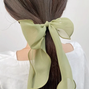 Elegant green chiffon bow hair tie with long ribbons worn by a model against white wall