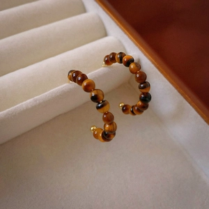 Macro view of C-shaped resin beaded hoop earrings with tiger eye texture and gold tips