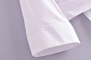Gros plan détaillé sur le poignet évasé et la texture en coton de la blouse cache-cœur blanche