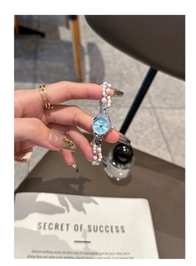 Silver pearl bracelet watch with a small round blue dial shown on a female wrist