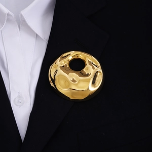 Detail shot of a golden textured round brooch on a black blazer and white shirt