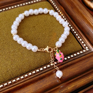 Detail of pearl bracelet featuring a gold-plated dragon fruit enamel charm and lobster clasp