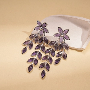 Detailed shot of purple glass flower earrings with leaf tassels on a stone pedestal