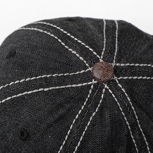 Macro detail of denim baseball cap crown with white contrast stitching and brown button