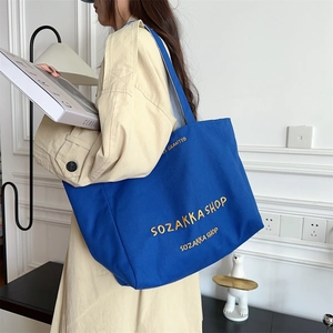 Detail einer blauen Canvas-Tasche mit gelber Stickerei und gestreiftem Innenfutter