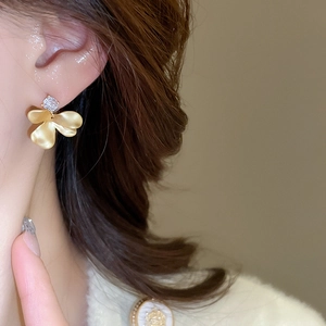 Macro view of matte gold flower earring with a sparkling zircon on a female model