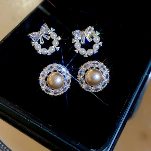 Close-up of bow and circular earrings with zircon and pearls in a black jewelry box