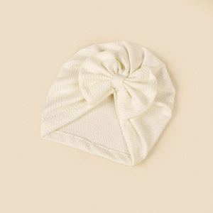 Detail showing the white knitted texture and large handmade bow of the infant turban hat