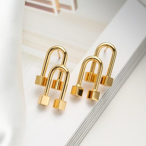 Minimalist gold-plated U-shaped earrings with cube charms on white silk fabric