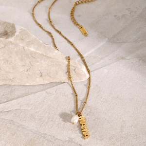 Macro detail of 18k gold plated MAMA necklace featuring freshwater pearl on stone texture