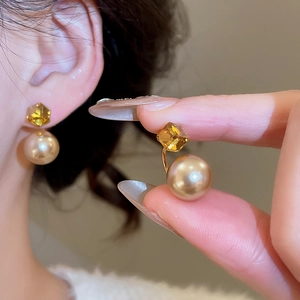 Detail showing gold earrings with champagne pearl and amber crystal on model's ear