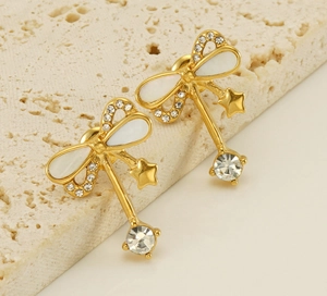 Macro detail of golden bow earrings with mother of pearl and dangling crystal star