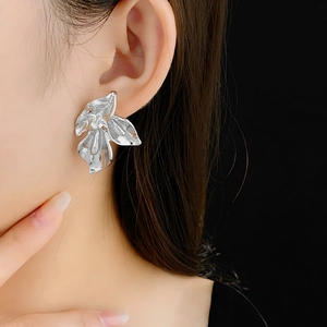 Détail de boucles d'oreilles pétales argentées montrant la texture et l'éclat sur modèle