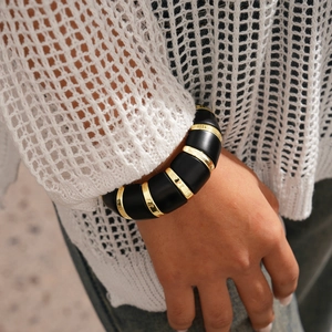 Détail d'un bracelet épais en acrylique avec maillons dorés sur une manche en tricot blanc