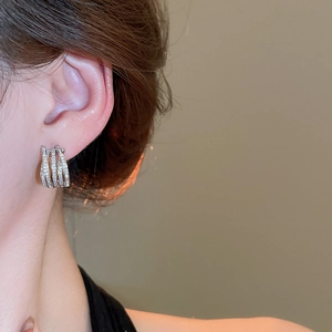 Detailed close-up of zircon-encrusted multi-layer crisscross hoop earrings on a model