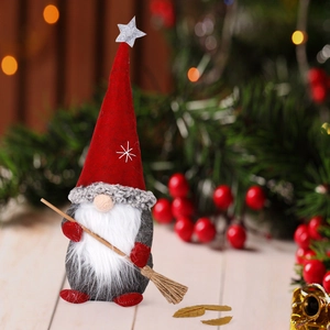 Christmas gnome doll with red hat and broom on wooden surface with festive bokeh background
