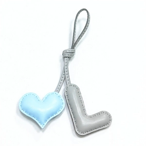 Detail of handmade leather bag charm featuring a light blue heart and grey letter L pendant