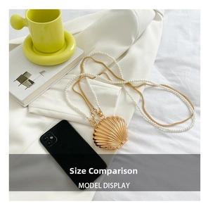 Mini golden shell evening bag with pearl chain shown next to a smartphone for size comparison