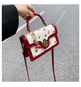 Detail of red and white crossbody bag featuring cherry print and metal flower clasp