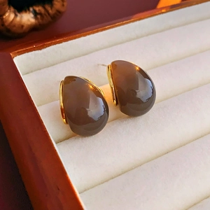 Macro shot of brown teardrop resin earrings with gold metal trim in a velvet jewelry box