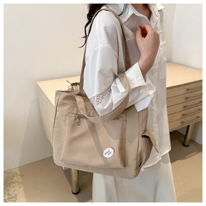 Detail of beige canvas tote bag with front pocket showing good luck label and zippers