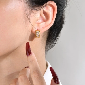 Detail shot of a gold hoop earring with a rectangular zircon worn by a female model