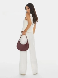 Detail of the deep burgundy leather crescent moon bag worn with a white sleeveless top
