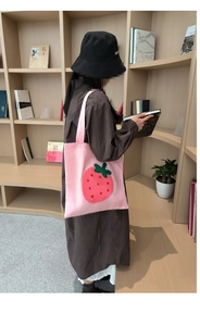 Detail view of pink canvas tote bag with a large plush strawberry embroidery pattern