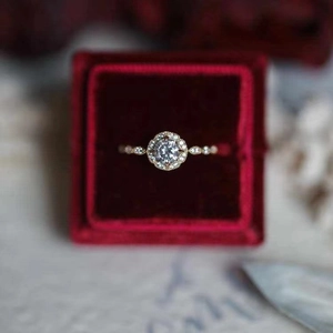Elegant gold halo ring with a bright round center stone in a luxury red velvet box