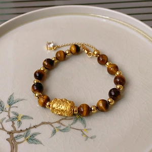 Close-up of tiger eye bead bracelet with golden mantra cylinder and extension chain