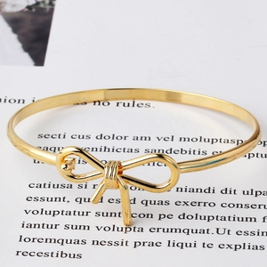 Dettaglio di un bracciale rigido dorato con nodo a fiocco su sfondo minimalista