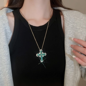 Vue détaillée d'un pendentif croix dorée avec pierres vertes et strass sur un mannequin