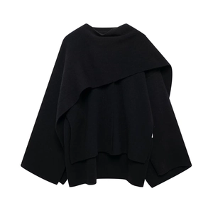Gros plan du manteau poncho noir asymétrique en tricot montrant la texture