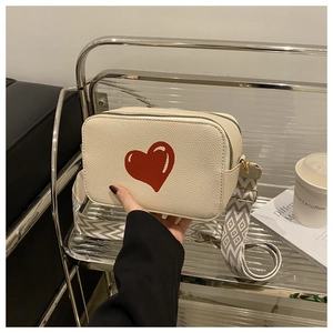 Detail of cream crossbody bag with red heart and patterned woven shoulder strap