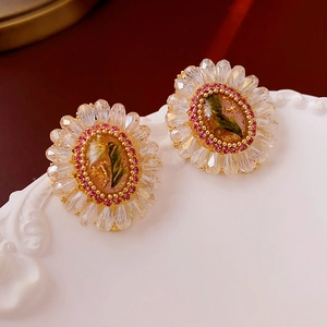 Macro detail of oval crystal flower earring featuring real green plants and gold leaf