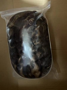Detail view of long wavy brown hair wig with highlights inside clear plastic packaging