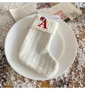 Detail of white knitted Christmas stocking with red embroidered letter A on a snowy background