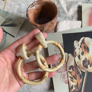 Close-up of bamboo style hoop earrings with resin accents held in hand against rustic decor