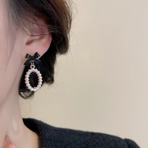 Close-up of elegant black bow earrings with pearl pendant shown on model ear