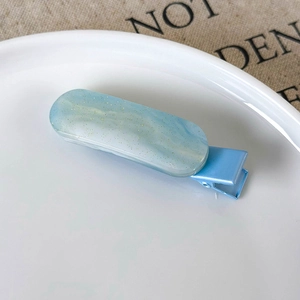Close-up of a blue glitter resin oval hair clip on a white ceramic plate edge
