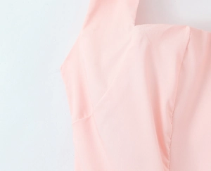 Detail of light pink woven fabric showing clean neckline and shoulder strap seams