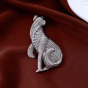 Detailed close-up of a silver cat brooch with geometric textures on dark red satin fabric