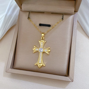 Close-up of a gold-tone cross necklace with white crystals in a beige jewelry box