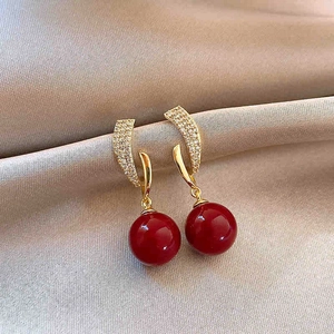 Macro detail of gold-plated earring with clear zircons and glossy dark red sphere pendant