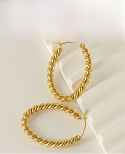 Detailed macro view of golden twisted hoop earrings on white stone background