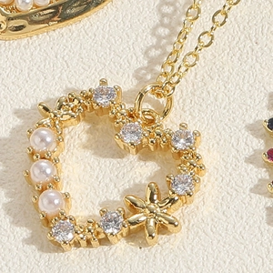 Close-up of heart pendant with gold plating, pearls, zircons and floral detail